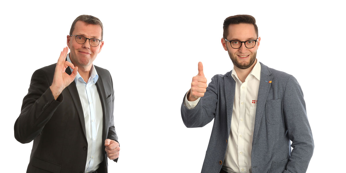 Herr Unterburger und Herr Zech stehen nebeneinander, einer zeigt das Zeichen für 'okay', der andere gibt einen Daumen hoch und lächelt.